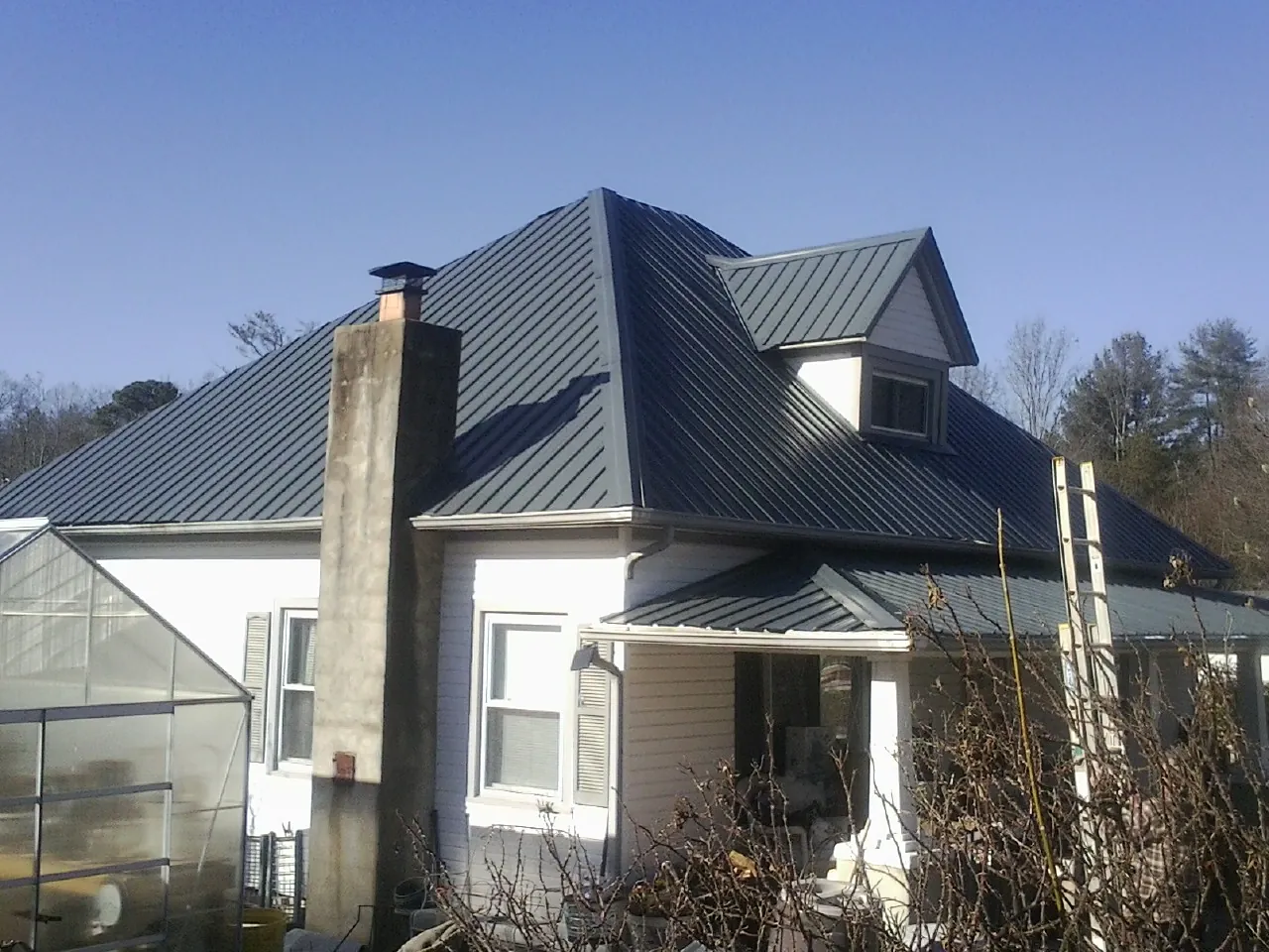 Dark blue standing seam metal roof on a white farmhouse with dormer — Slate & Tile Roof Repair by Roofing Brothers in Port Neches