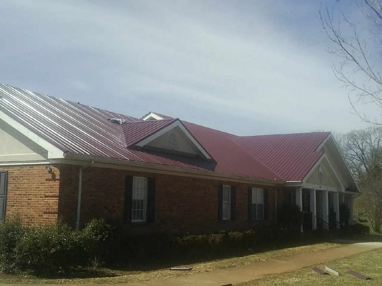 Red metal roof with gabled entries on a long brick building, from a Hail Damage Roof Repair job in Port Neches