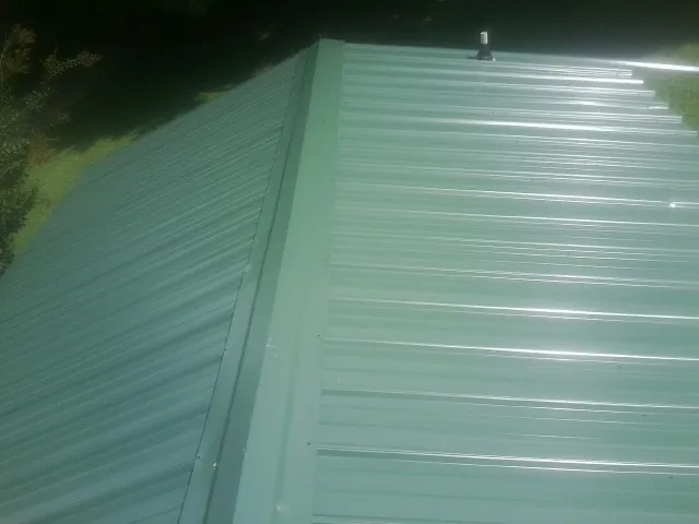 New green metal panels meeting at the ridge of a roof — Flat Roof Repair work by our crew in Port Neches