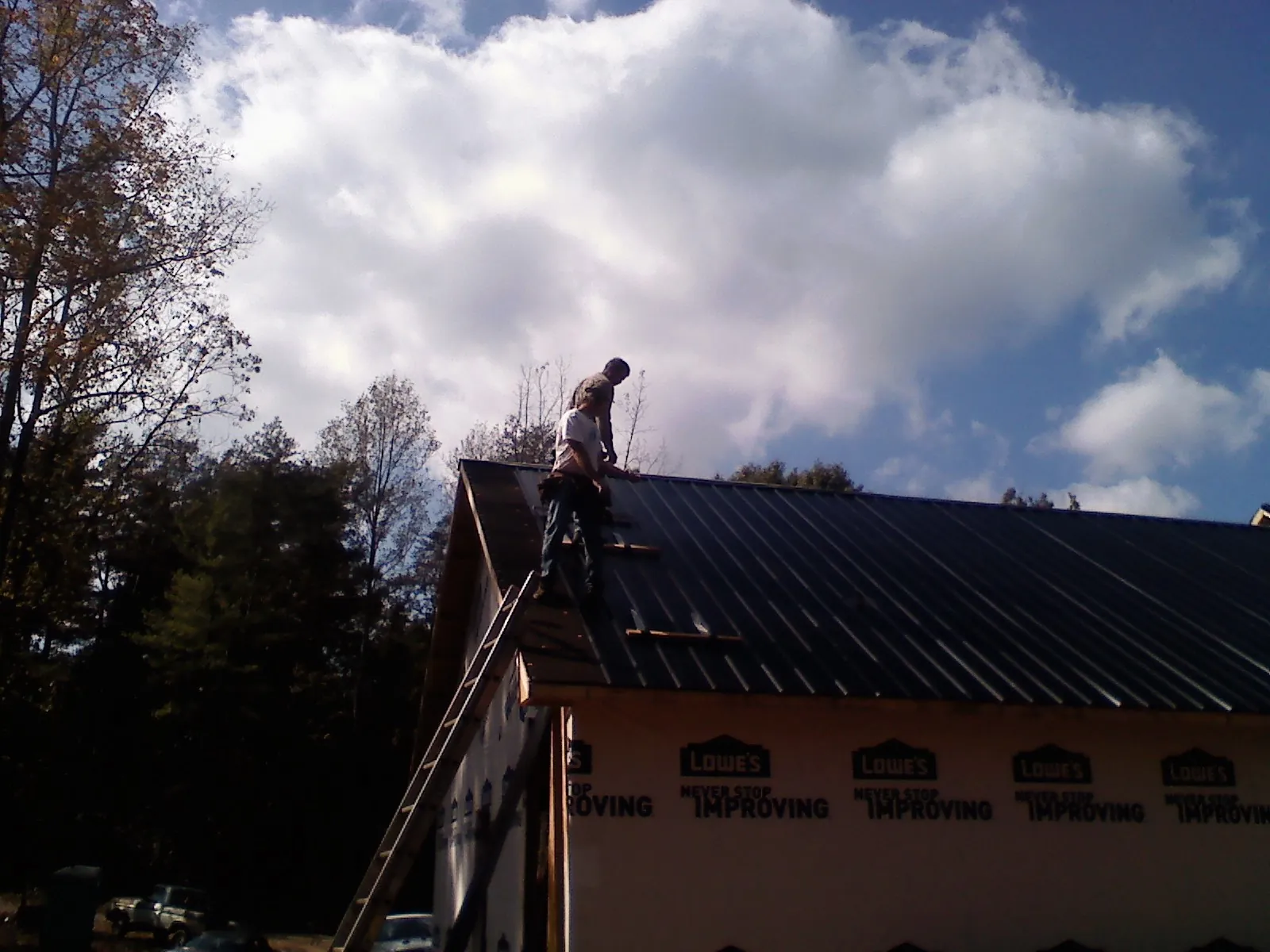 Roofer fastening dark metal panels high against a cloudy sky, from a Roof Inspection job in Port Neches