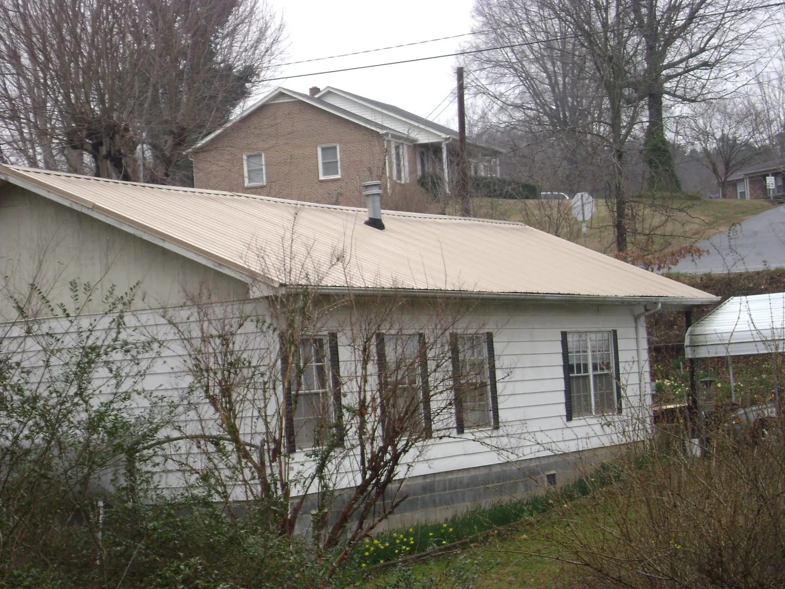 Tan metal roof on a white sided house set into a hillside — Commercial Roofing by Roofing Brothers in Port Neches