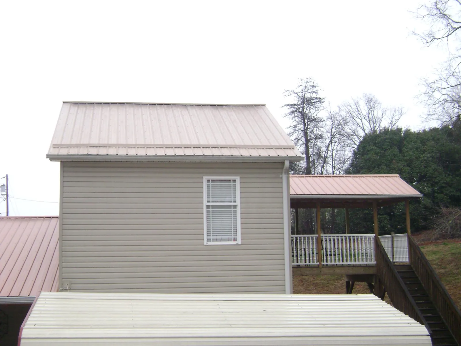 Tan metal roofs on a two story addition and attached porch, from a Roof Replacement job in Port Neches